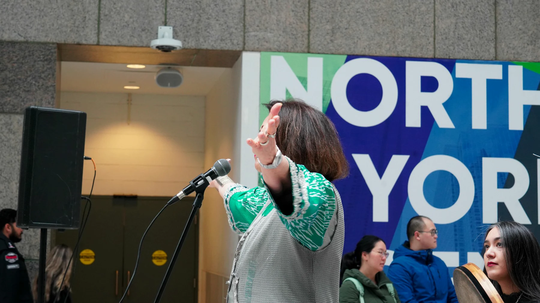 A speaker gestures while addressing a live audience with a microphone